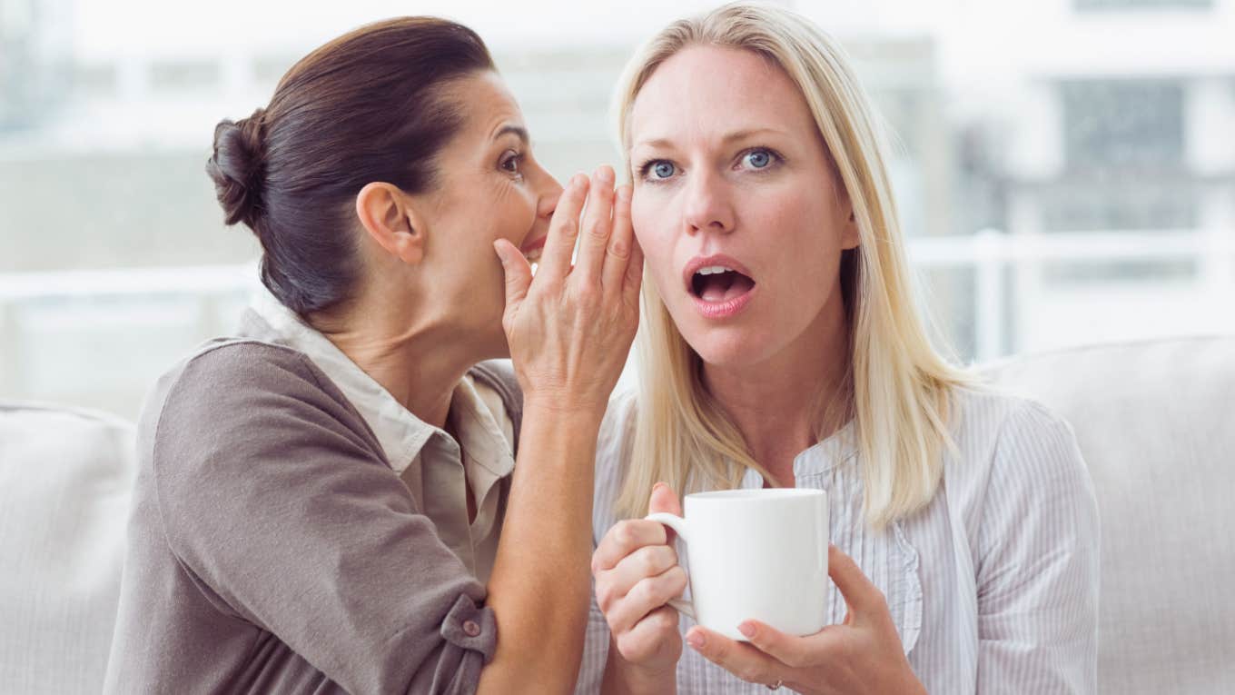 woman whispering secret into surprised woman's ear