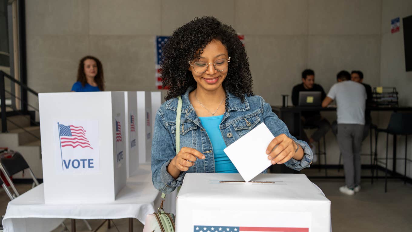 woman putting her ballot in a box after voting at a booth