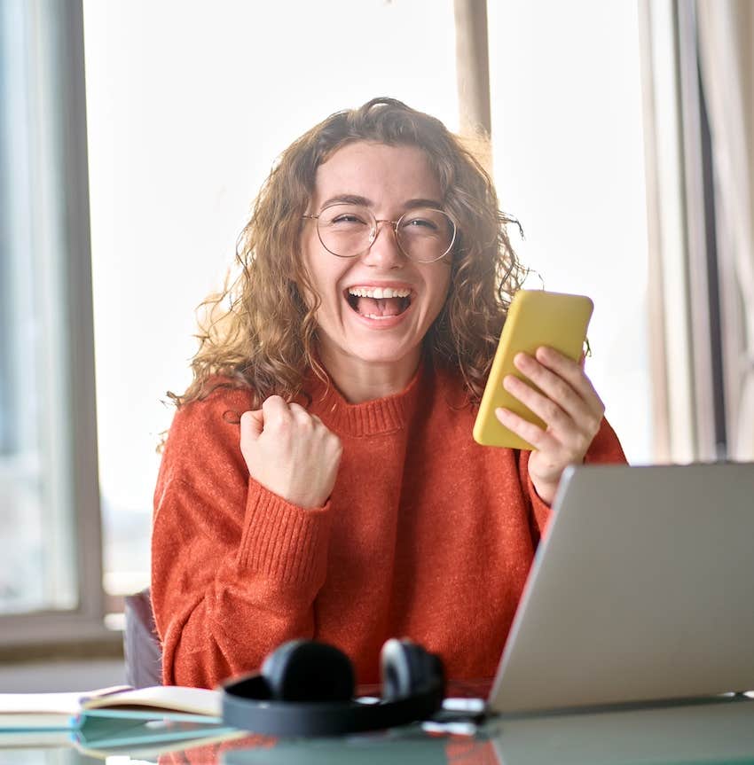 Excited woman looks at phone and feels a sense of winning