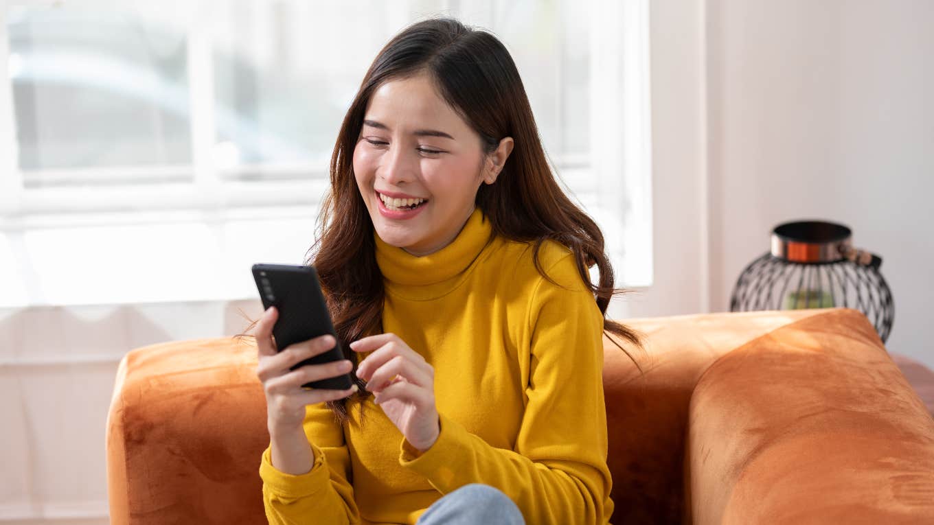 young woman smiling at phone sitting on couch