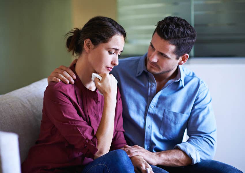 attentive husband comforts and holds anxious wife on couch at home