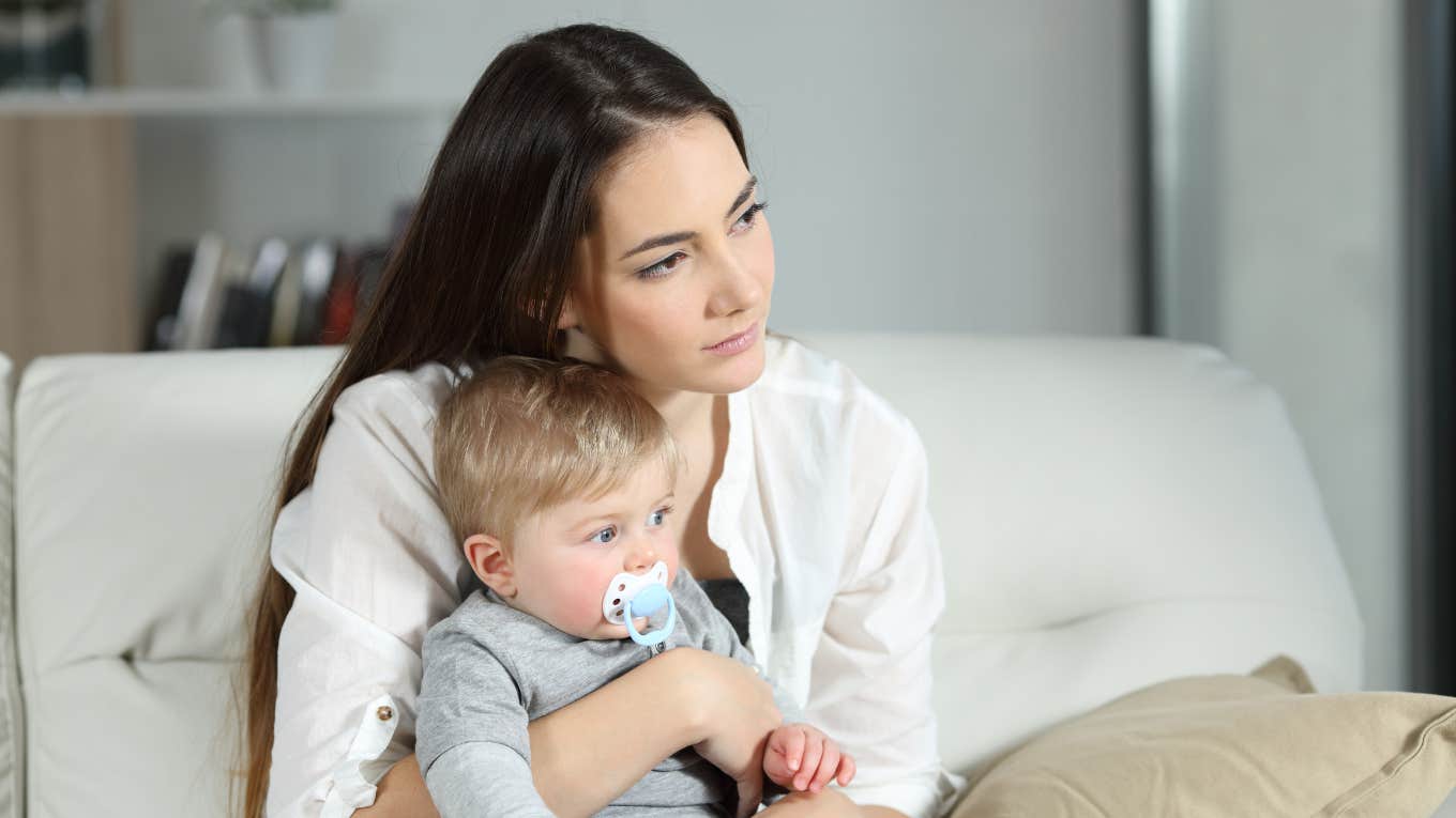 Mom holding toddler looking sad while sitting on a couch