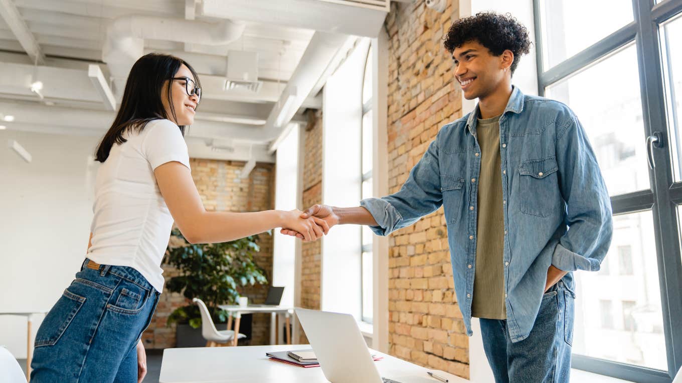 two co-workers shaking hands across a desk