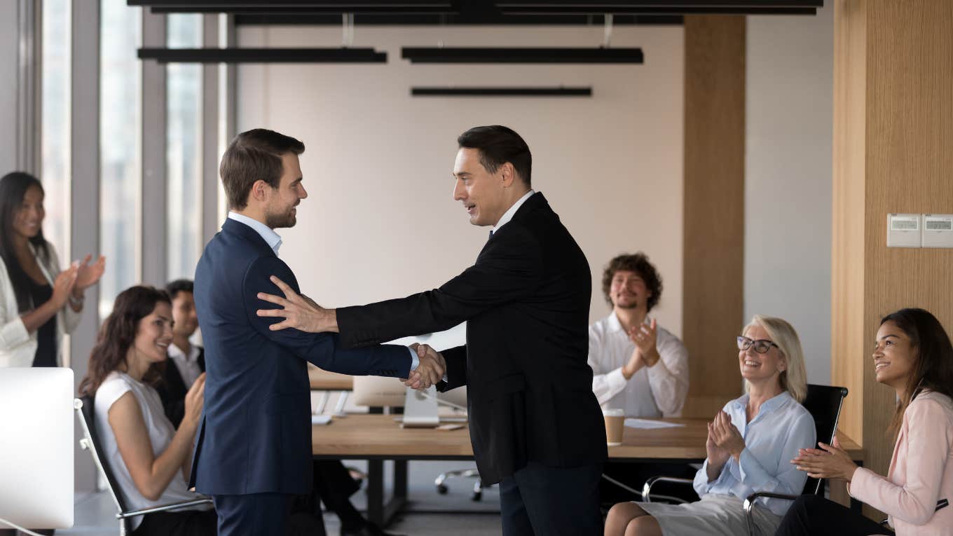 boss congratulating promoted employee with staff applauding