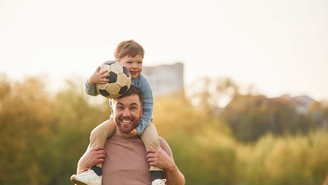 little boy holding a soccer ball on his dad's shoulders