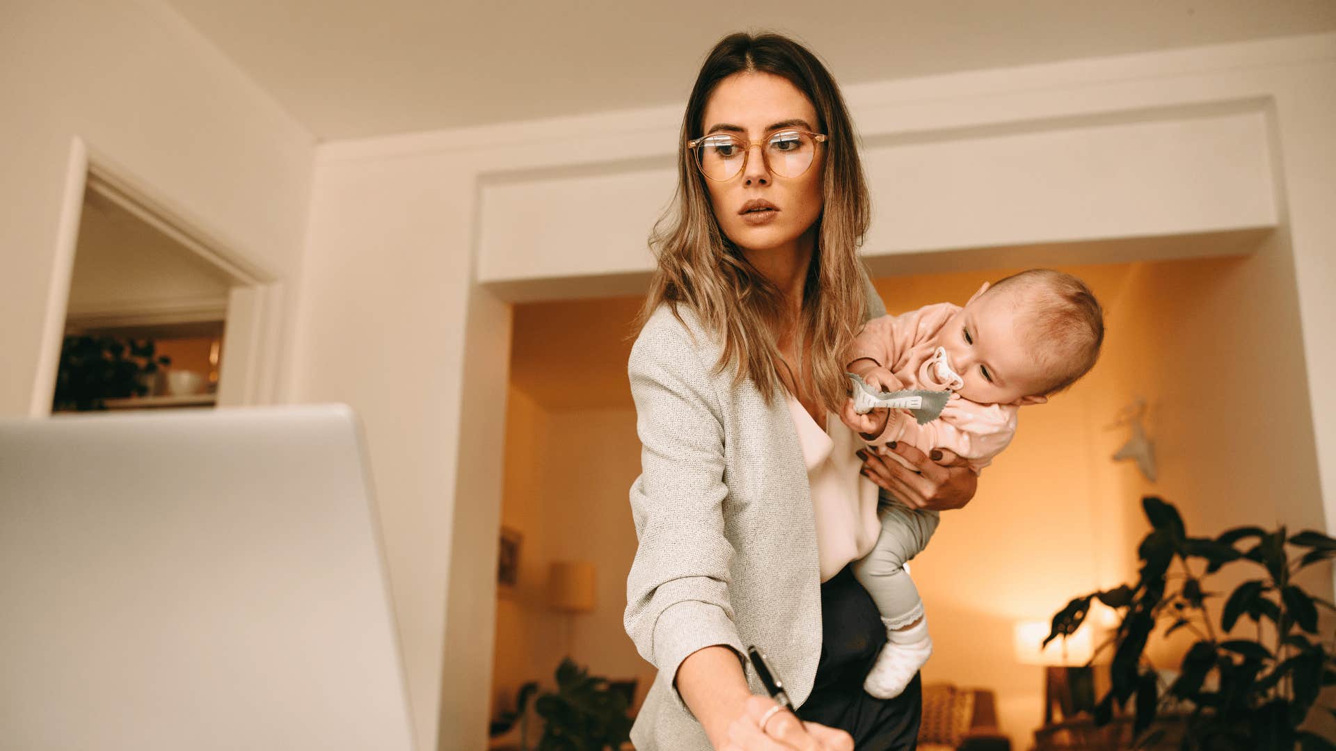 Woman holds child and makes notes while working on computer