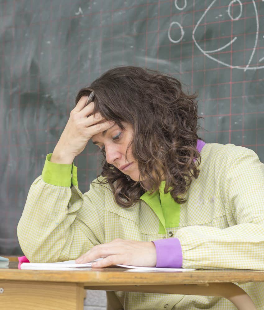 Exhausted teacher sitting at her desk with her head in her hand