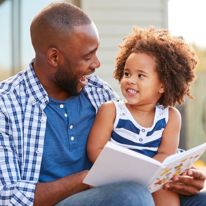 Father and daughter smiling while reading together.