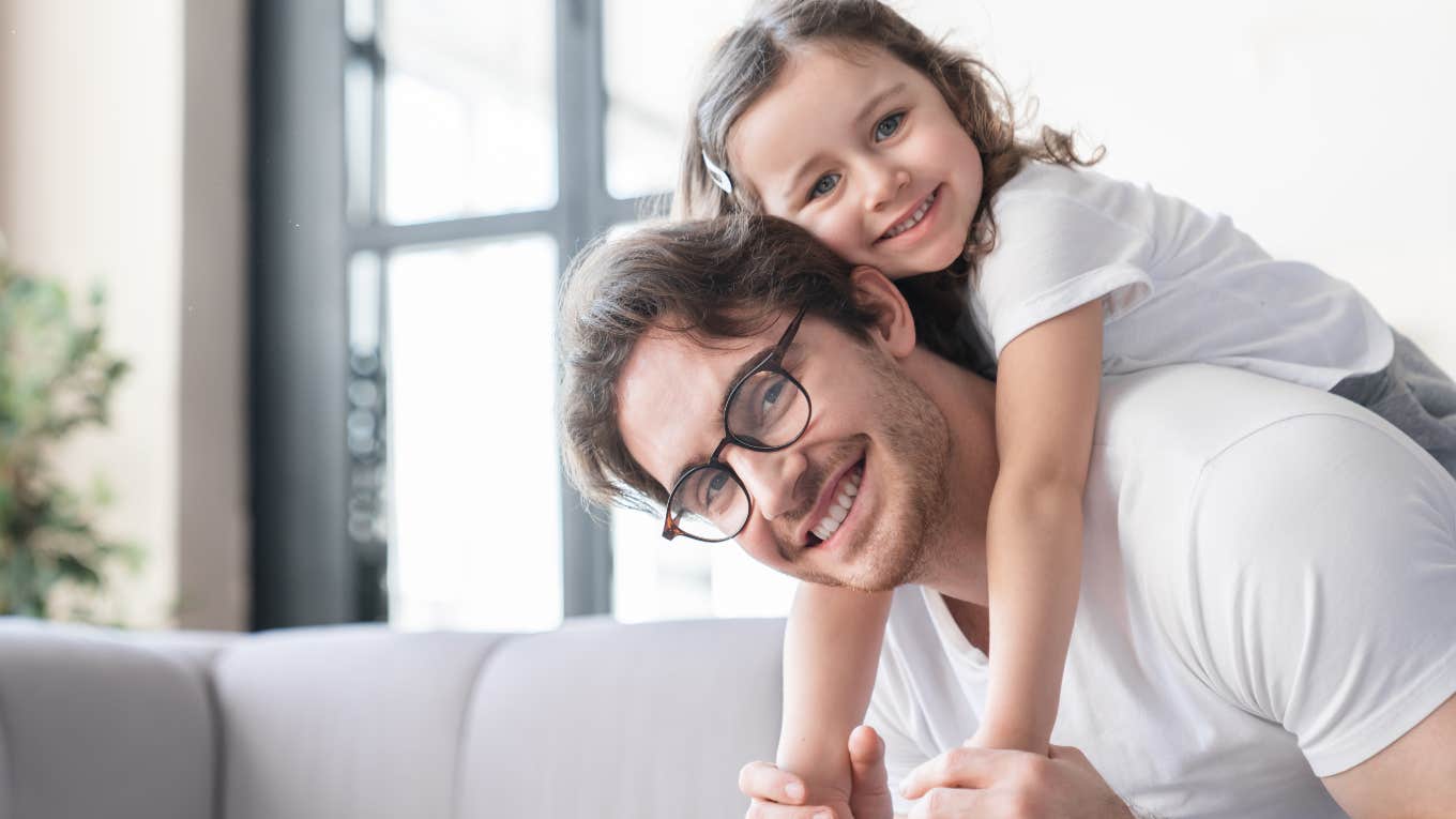 dad with young daughter on his back in front of couch