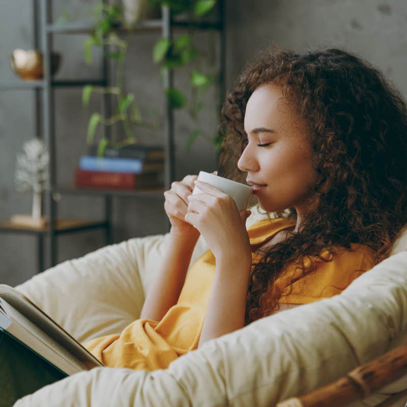 woman sipping from cup with eyes closed and book on lap