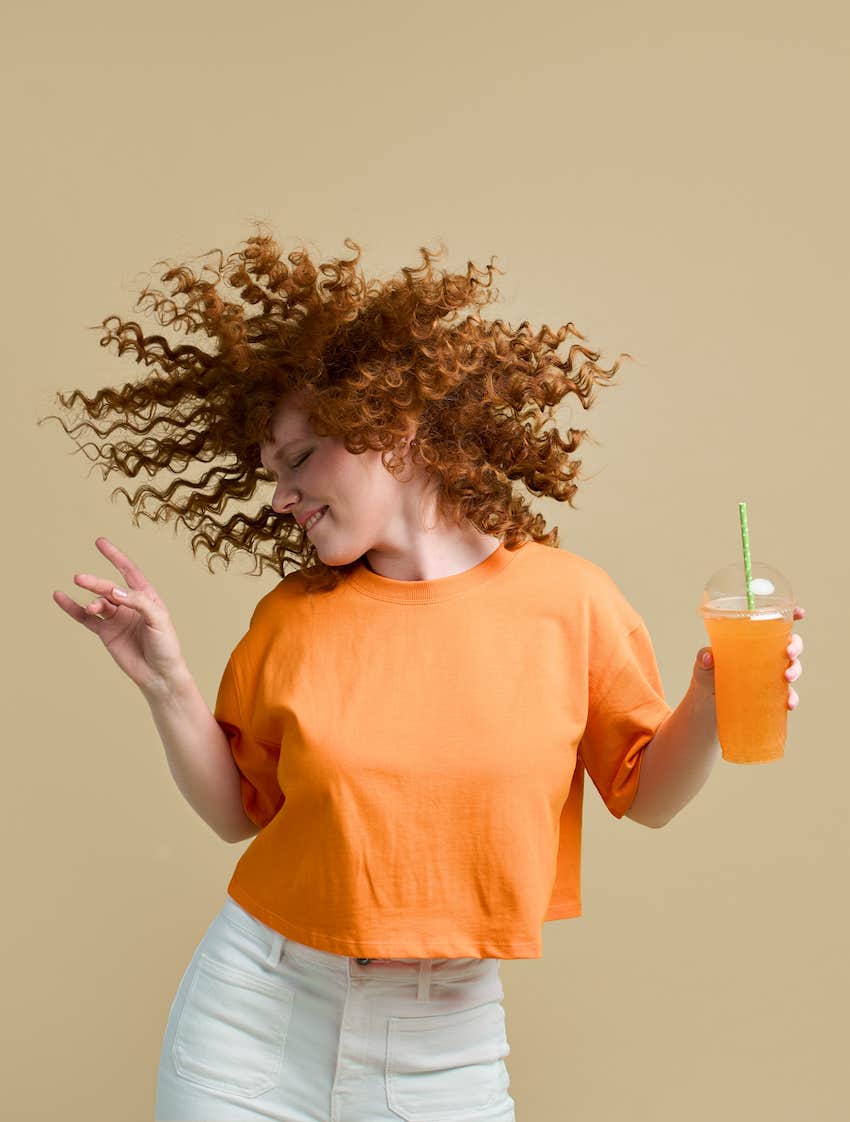 She dances joyfully holding cup of juice, her hair fans out above her head