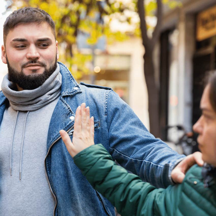 HE touches her shoulder, she puts up her hand to say "stop".