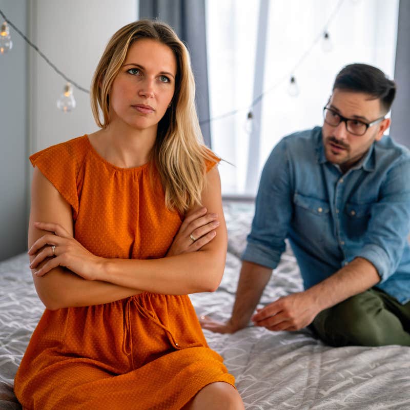 wife sitting with back to husband on bed during argument