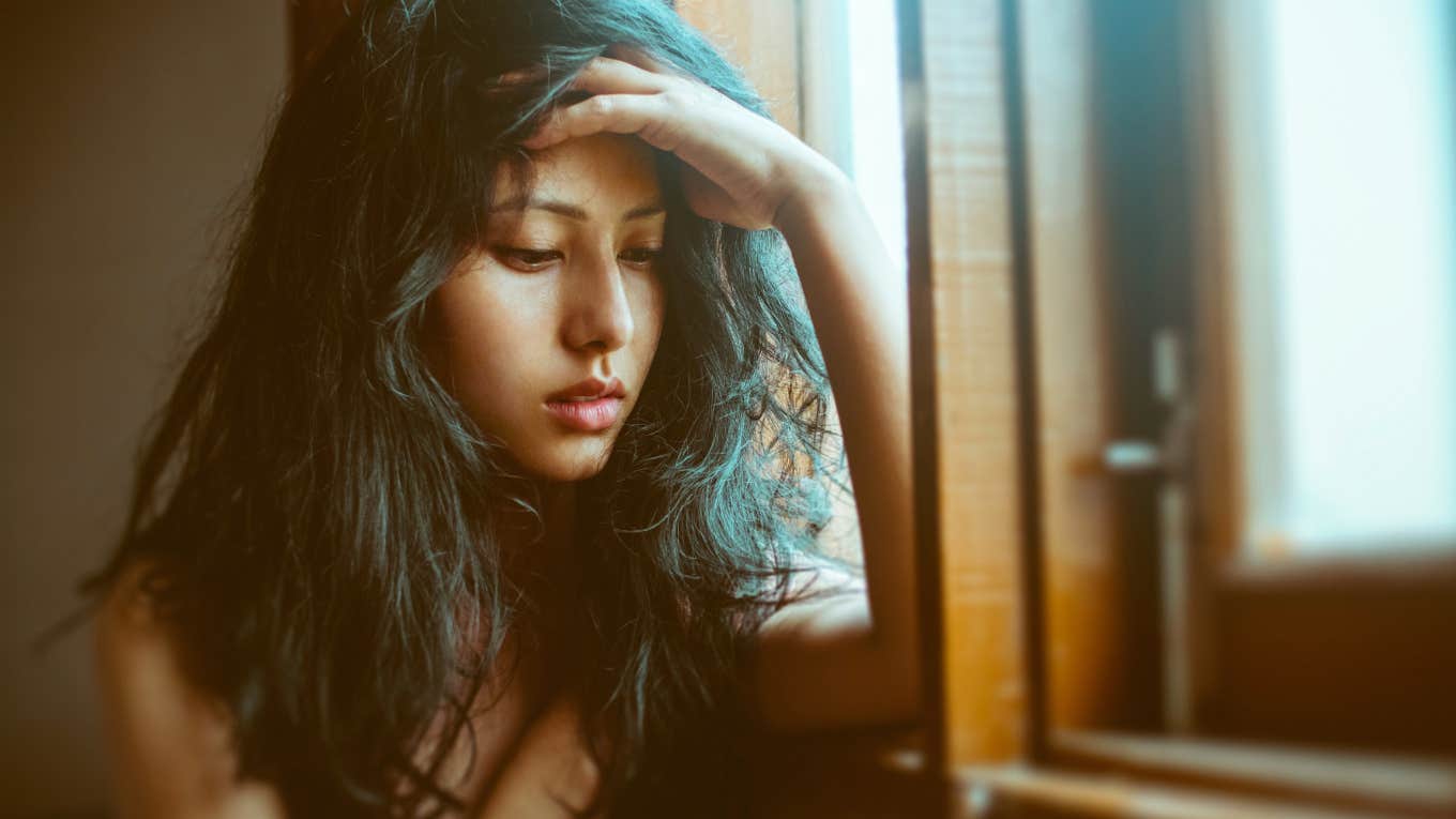 Sad woman standing by window with hand on head