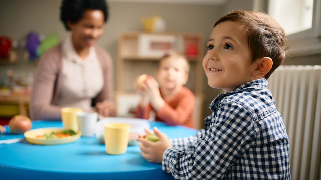 little boy having lunch with his friends and teacher at preschool.