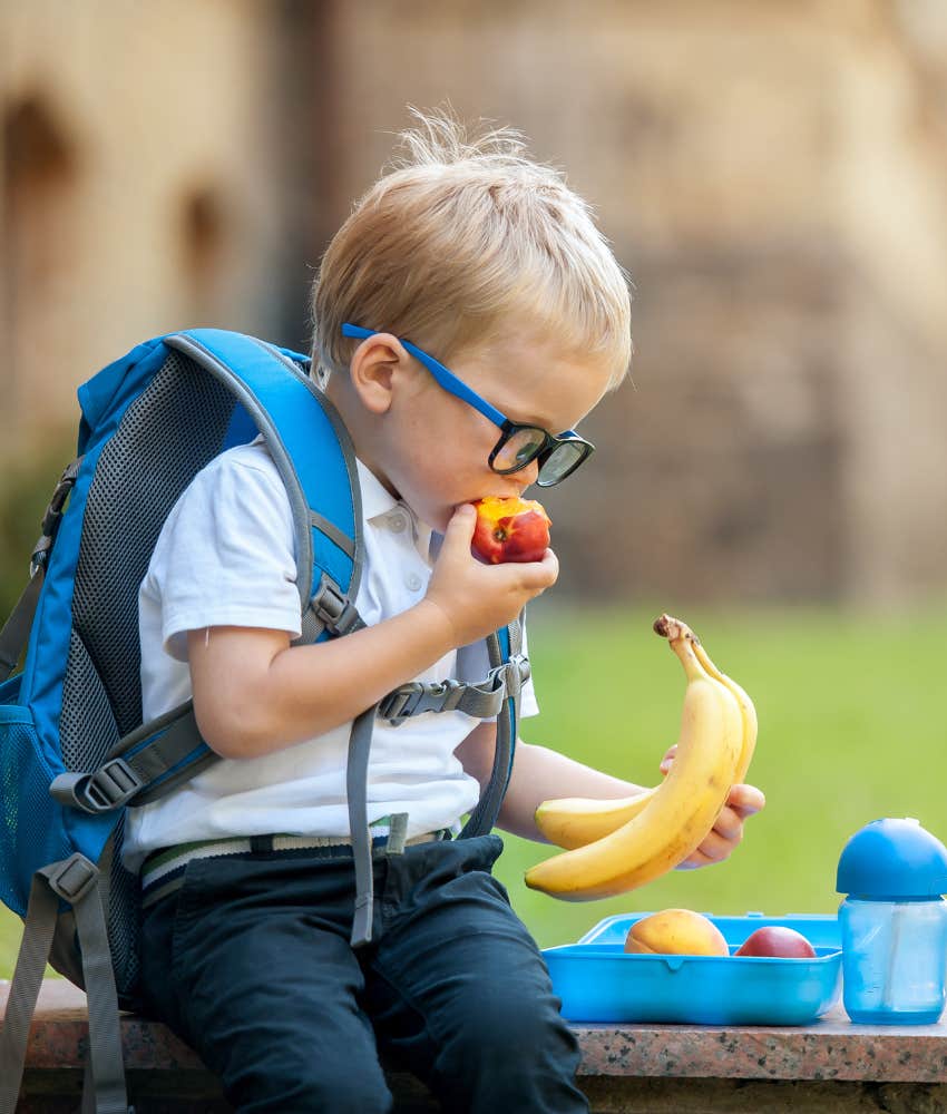 little boy wearing a backpack eating his school lunch