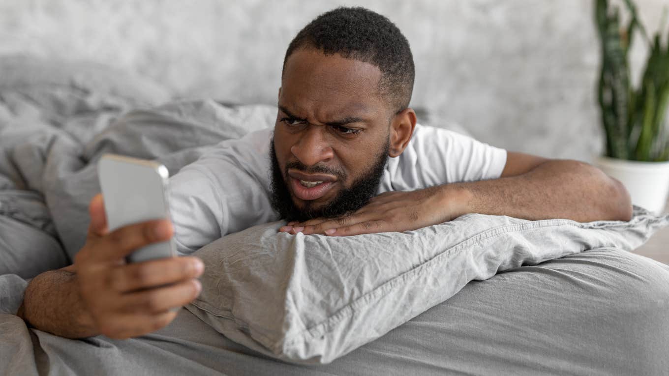 Man looking angrily at a text from his girlfriend on his phone. 