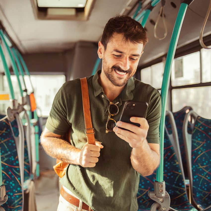 Man smiling on his phone on public transportation. 