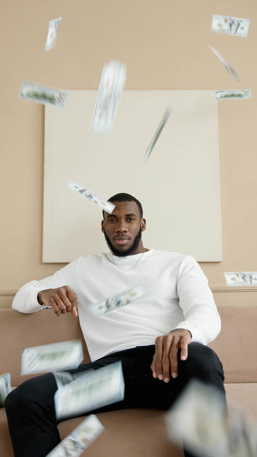 man sitting on couch with money floating in air around him