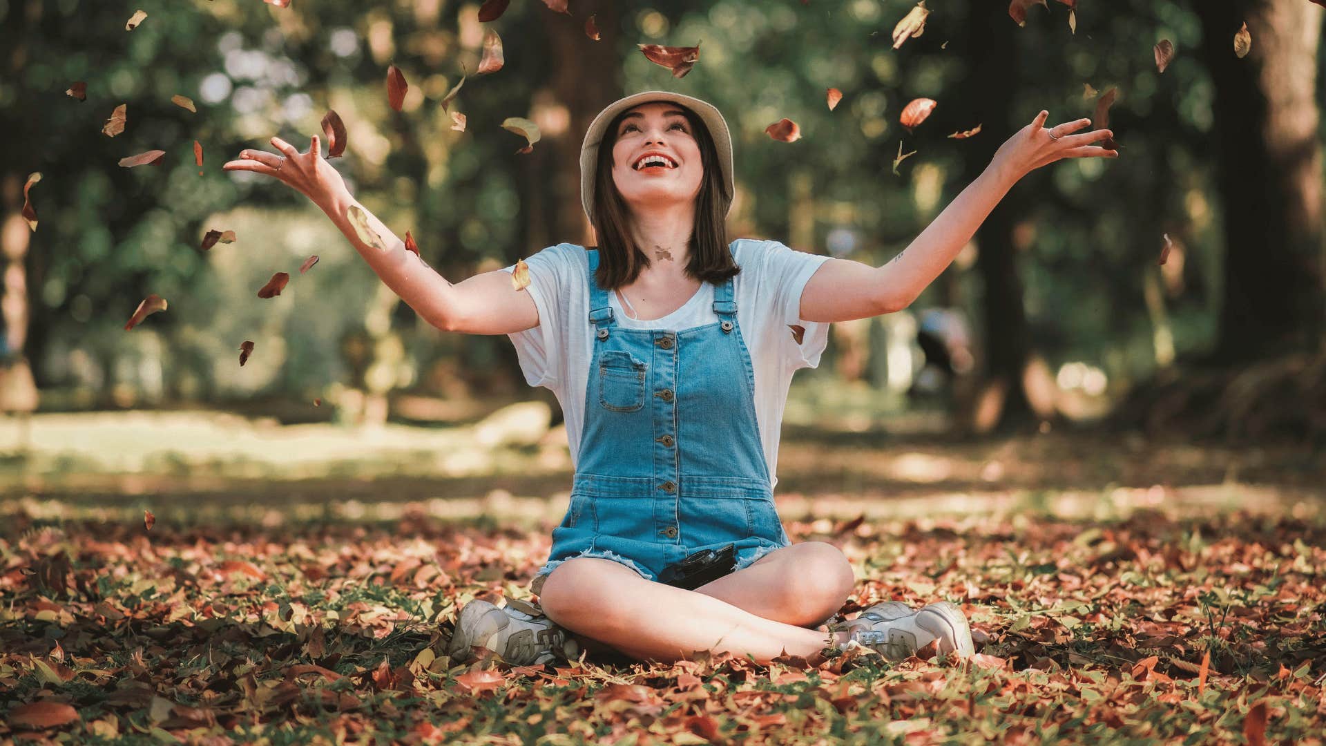 woman sitting down and tossing leafs