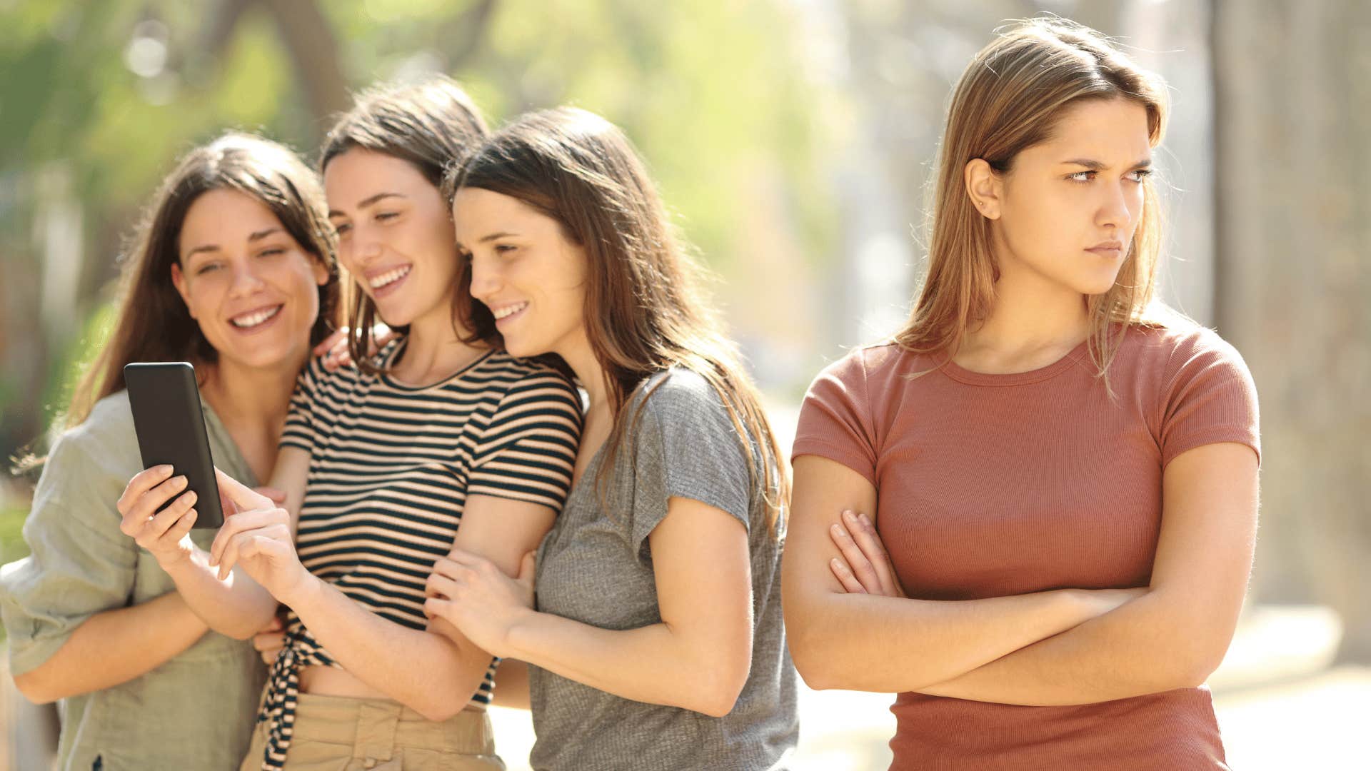 woman looking upset while group of friends stare at phone 