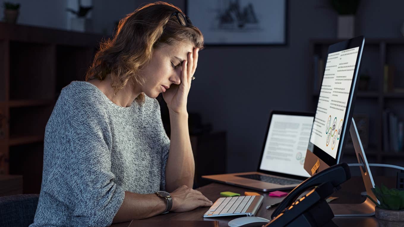 exhausted woman with eyes closed in front of computer at office