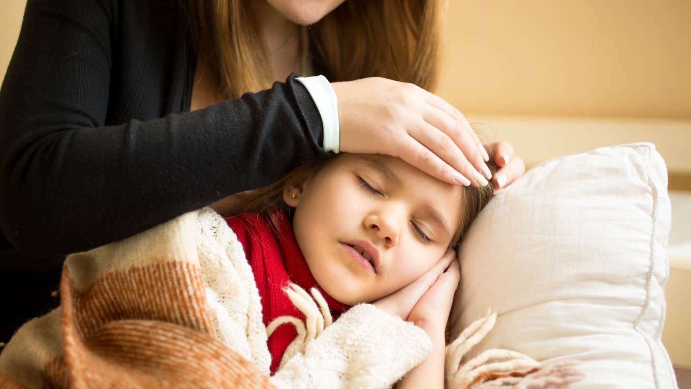 mom putting hand on the forehead of sick daughter sleeping 