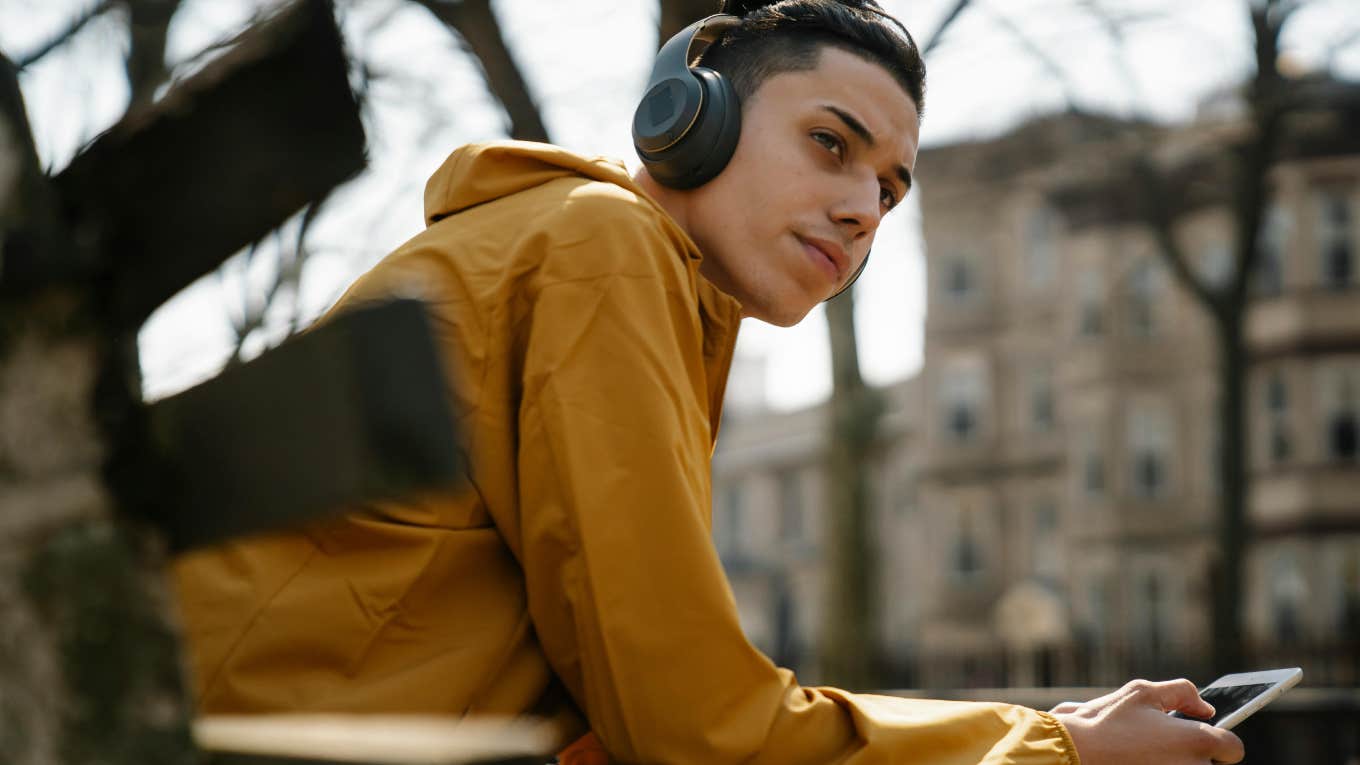 young man sitting on park bench with headphones and phone in hand