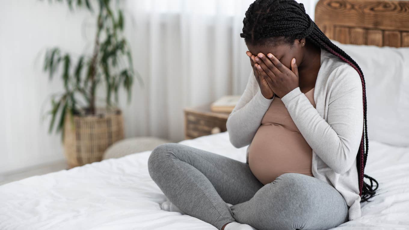 sad pregnant woman sitting on bed with head in her hands