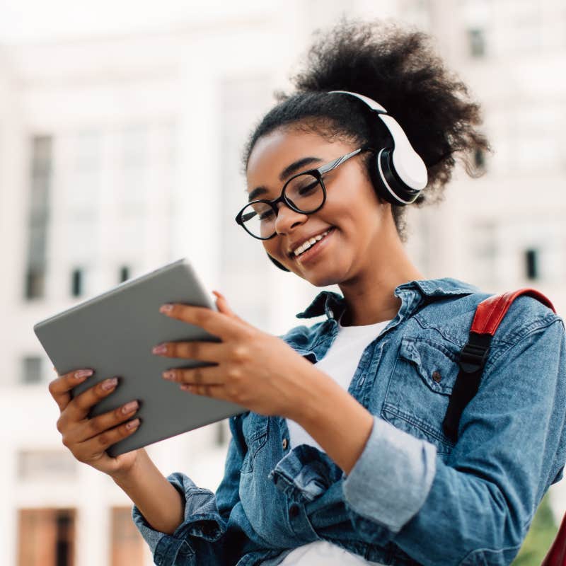 college student working on tablet with headphones on outside