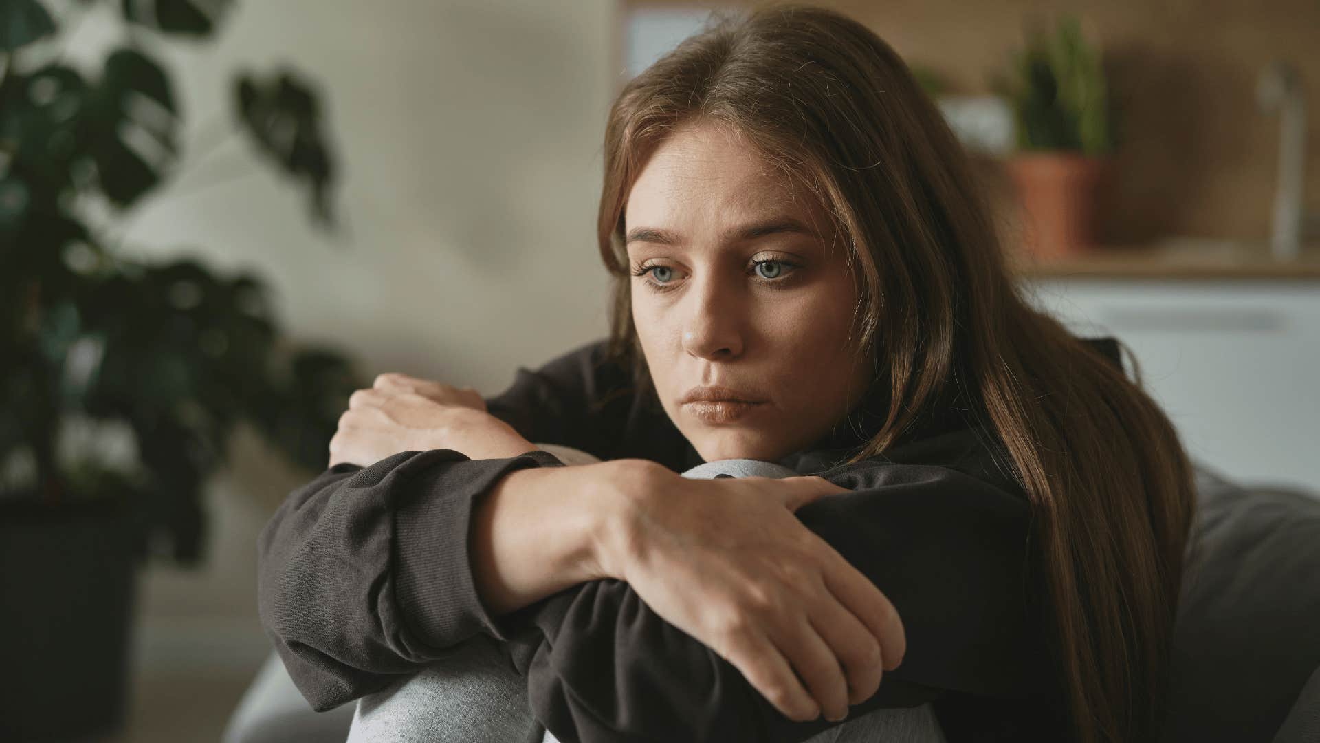 woman looking upset while hugging knees 