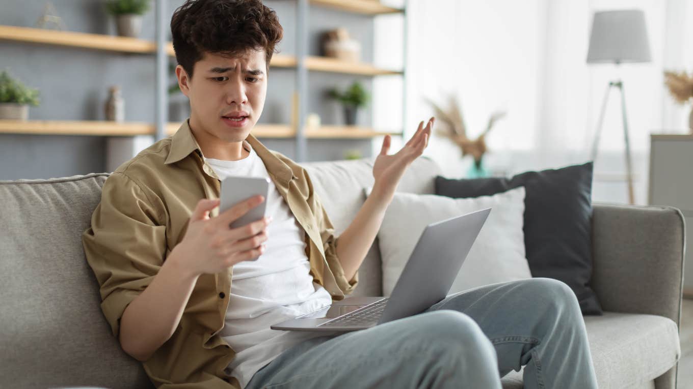 confused man sitting on couch with laptop looking at his phone