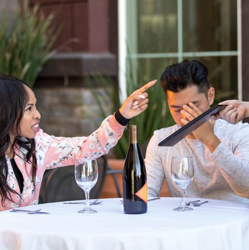 Woman pointing angrily at waiter while man is embarrassed 