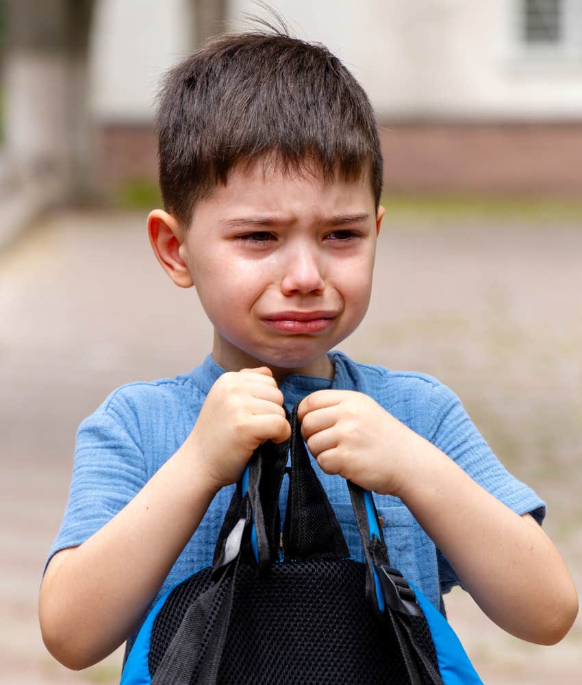 crying preschool student holding backpack