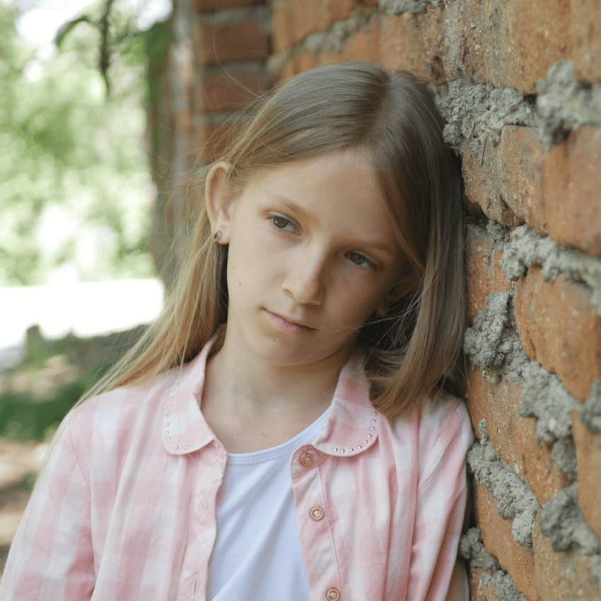 sad young girl leaning against brick wall