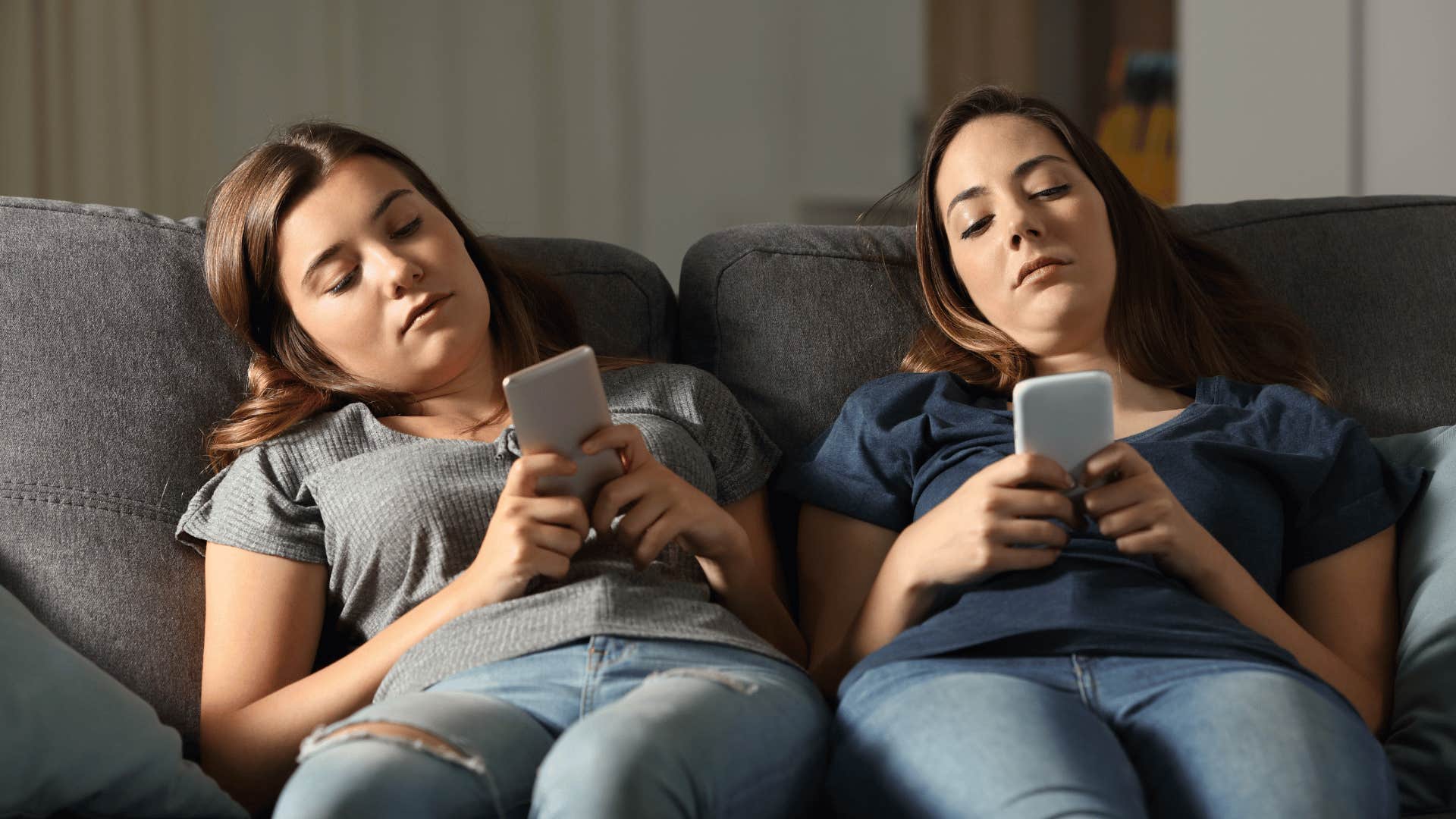 two women sitting on couch staring at phones looking bored 