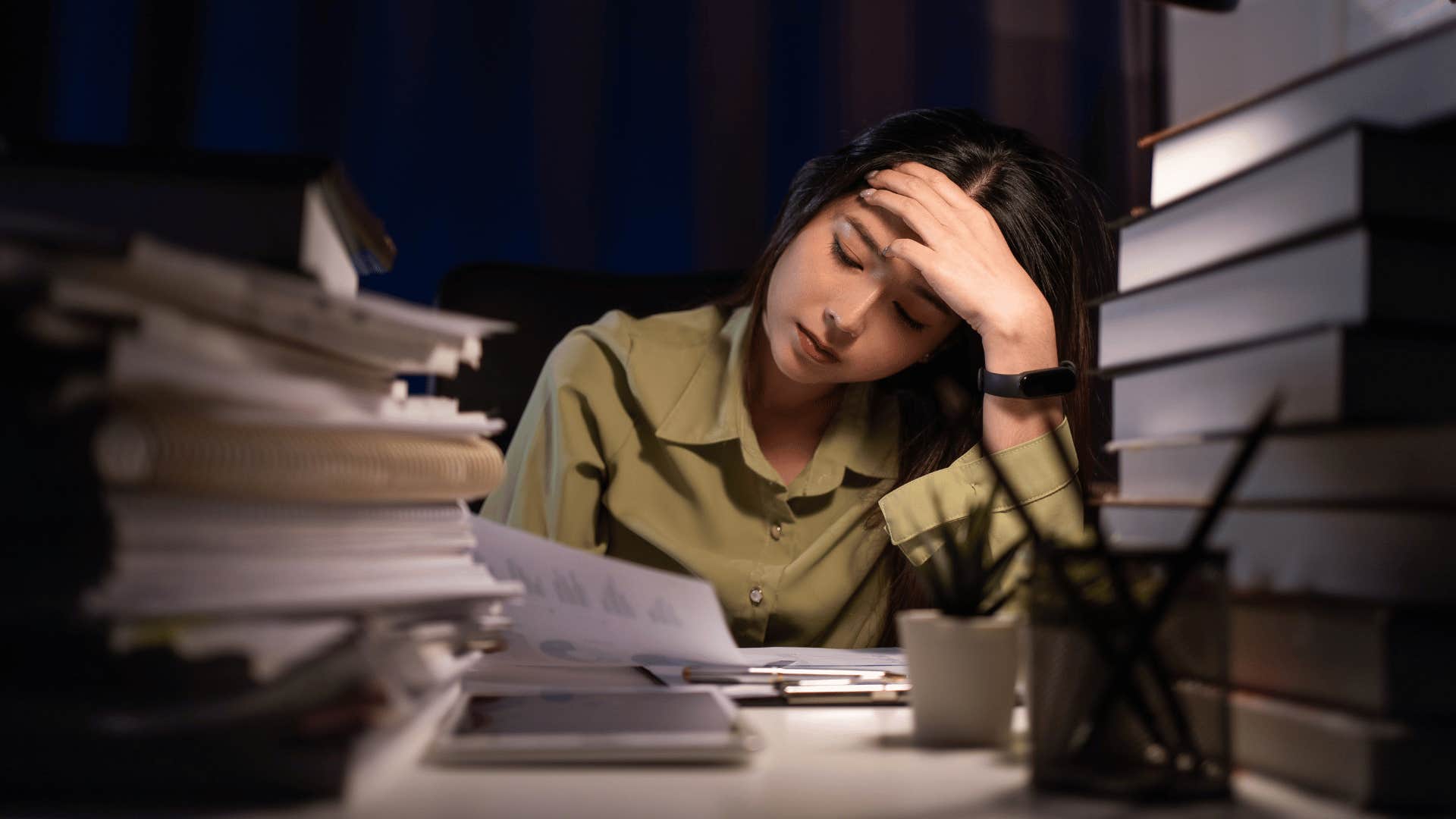 woman looking stressed with pile of books around her 