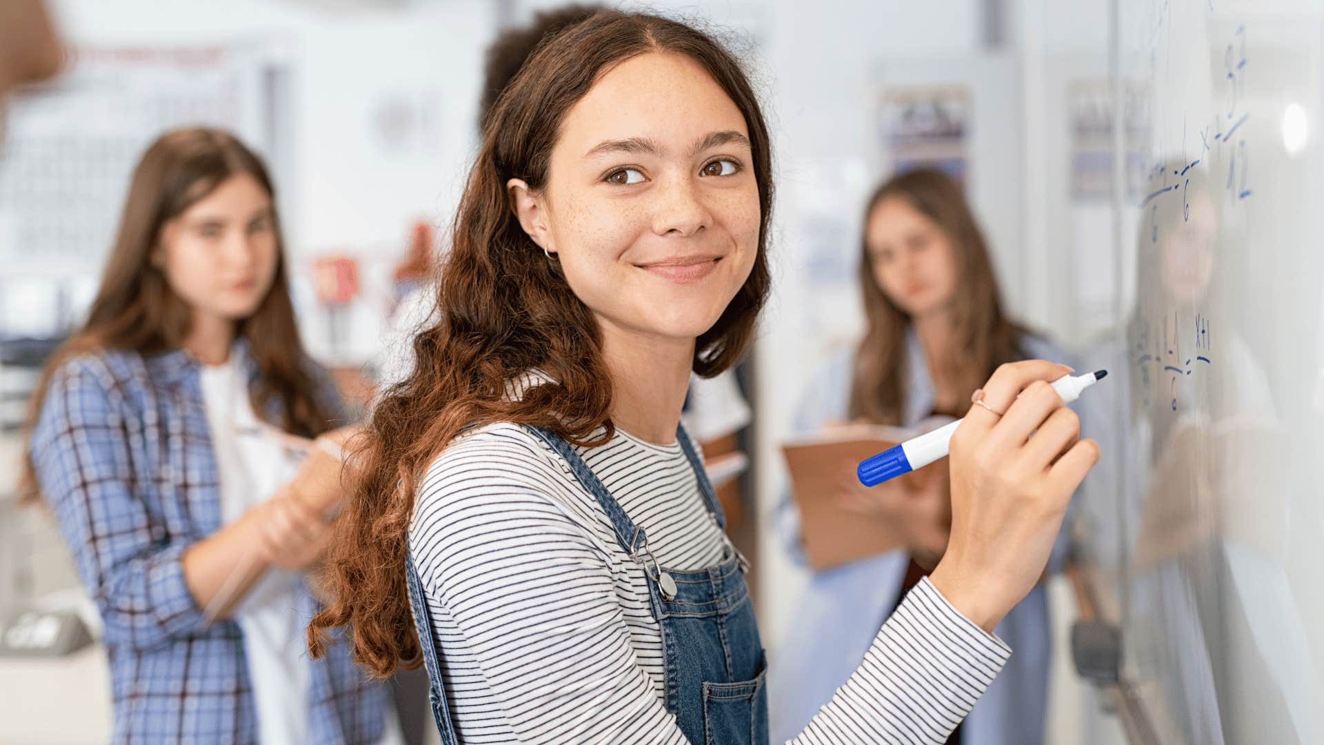 young woman solving problem on board while classmates watch 