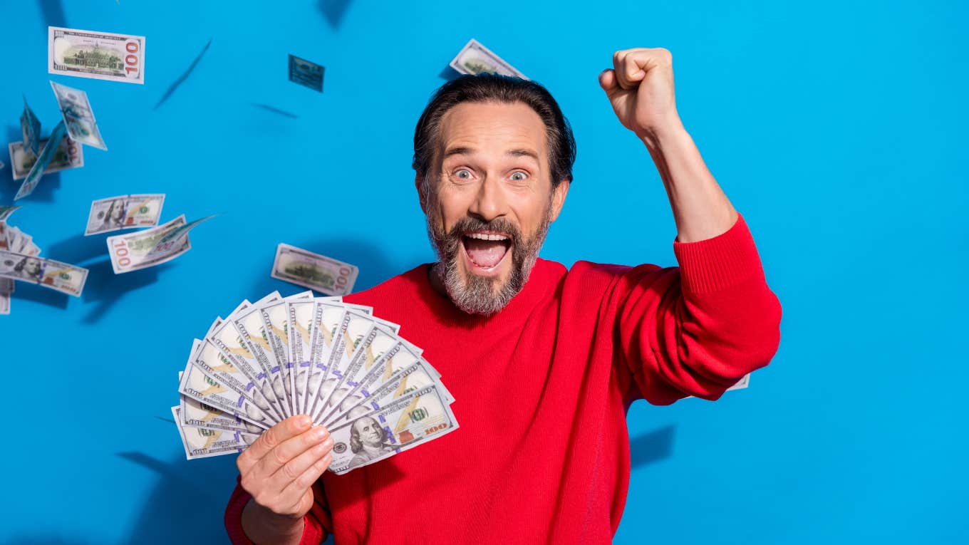 excited man holding lots of cash with more floating in the air around him