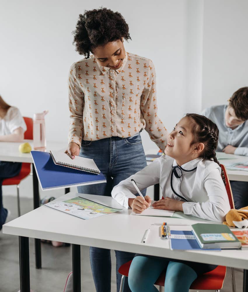 teacher standing next to students desk helping with assignment