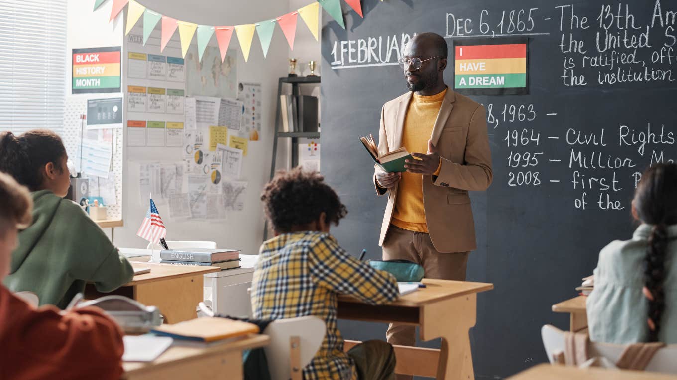 Teacher holding book at the front of an elementary school classroom