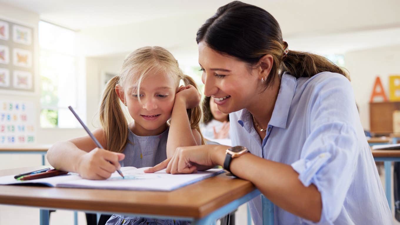 teacher helping little girl with assignment in classroom