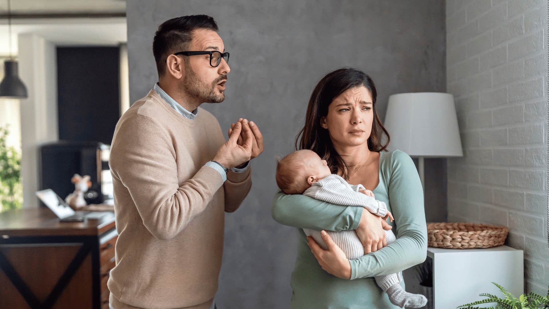 Upset man gestures at woman holding baby 