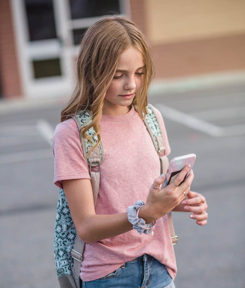 tween girl leaving school and reading her phone