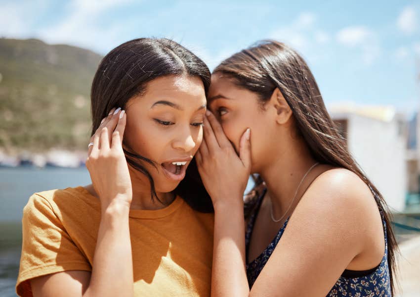 two friends whisper and gossip to each other outside