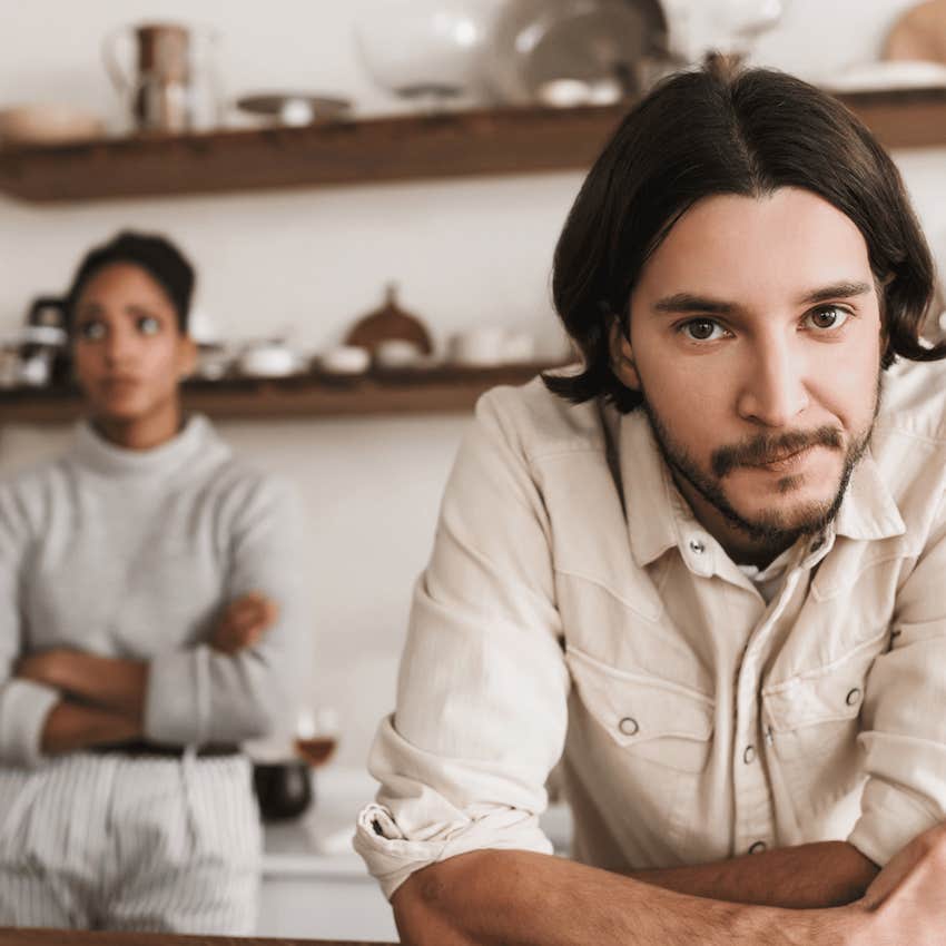 Uncertain man leans on counter while woman behind is defensive with arms across stomach