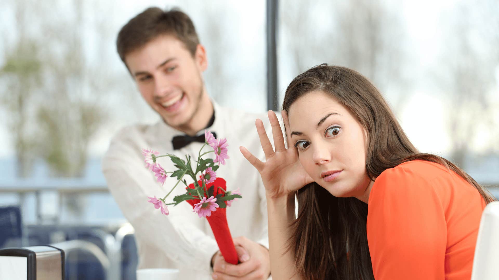 He hands her flowers, she looks away and hides her annoyed face