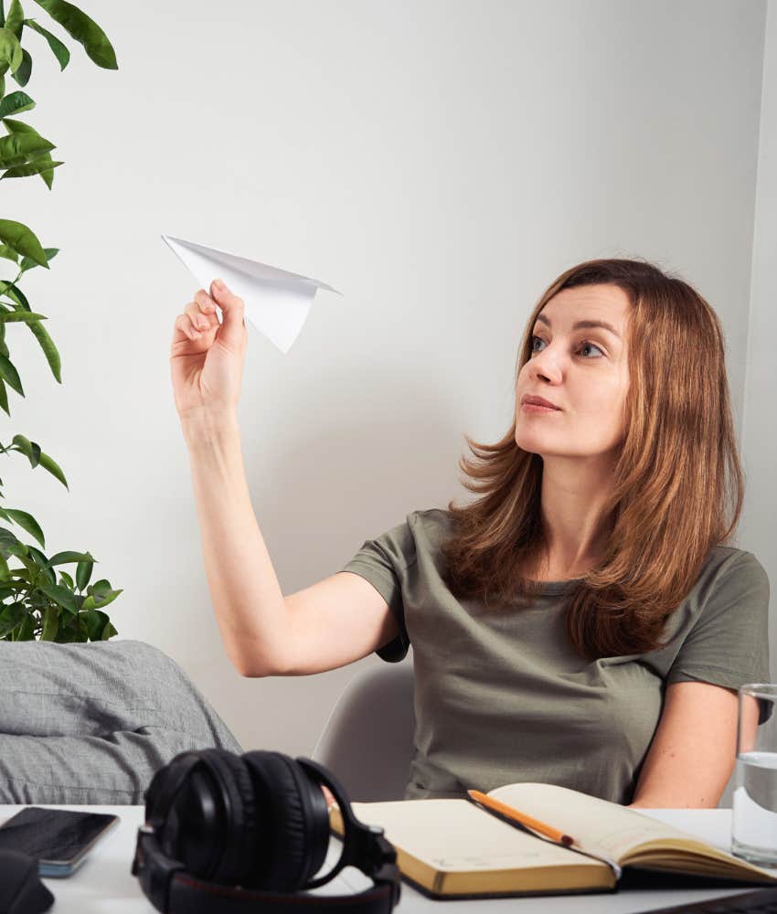 woman procrastinating at work with a paper airplane