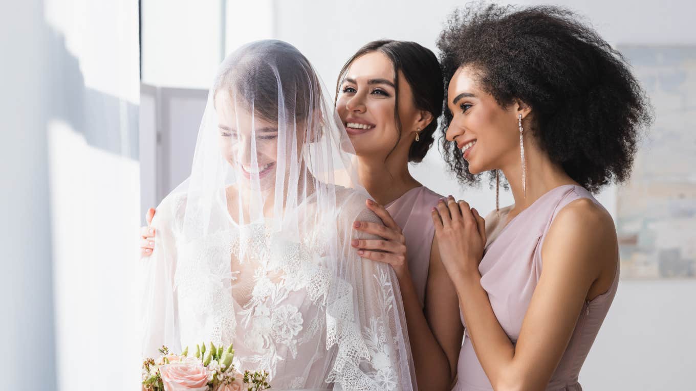 happy bride holding wedding bouquet near smiling bridesmaids