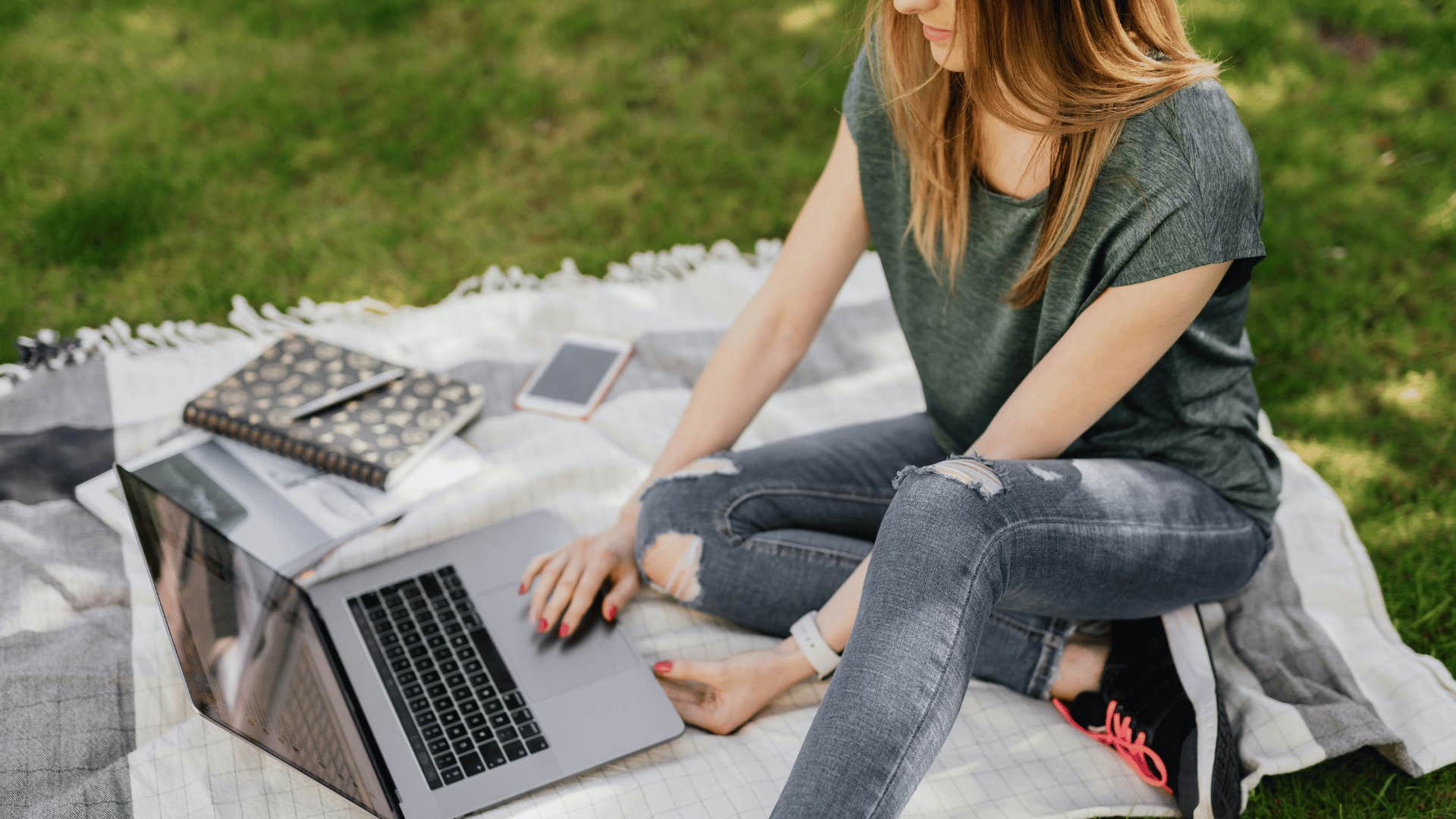 woman sitting on blanket outdoors working on laptop